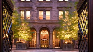 La entrada del hotel Lotte New York Palace, con un arco monumental, amplias ventanas e iluminación decorativa.