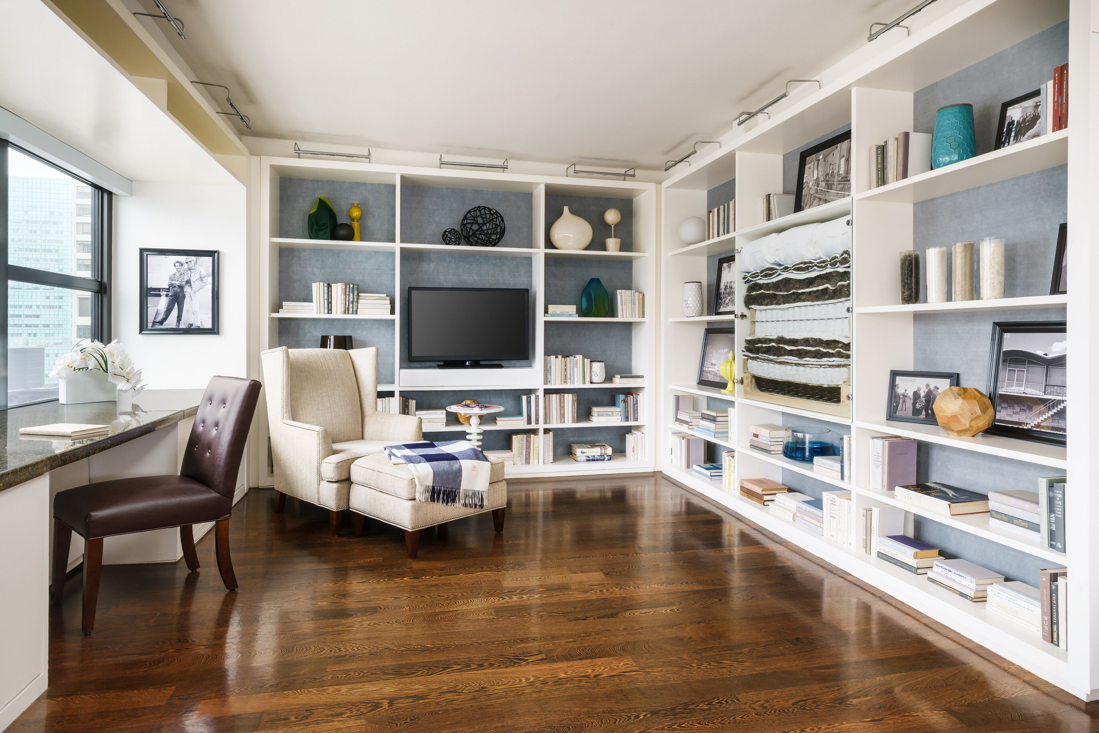A modern living room with a flat-screen TV, a comfortable armchair, a dining area with a wooden table, and a bookshelf filled with books and decorative items.