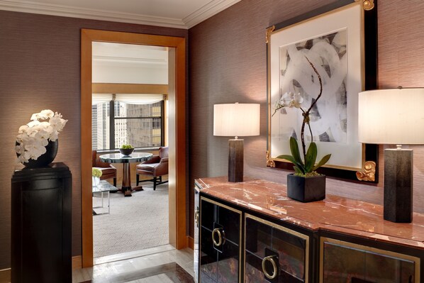 A hotel lobby with a marble reception desk, a framed abstract painting, a potted plant, and a view of the cityscape through a glass door. - The Towers at Lotte New York Palace (New York)