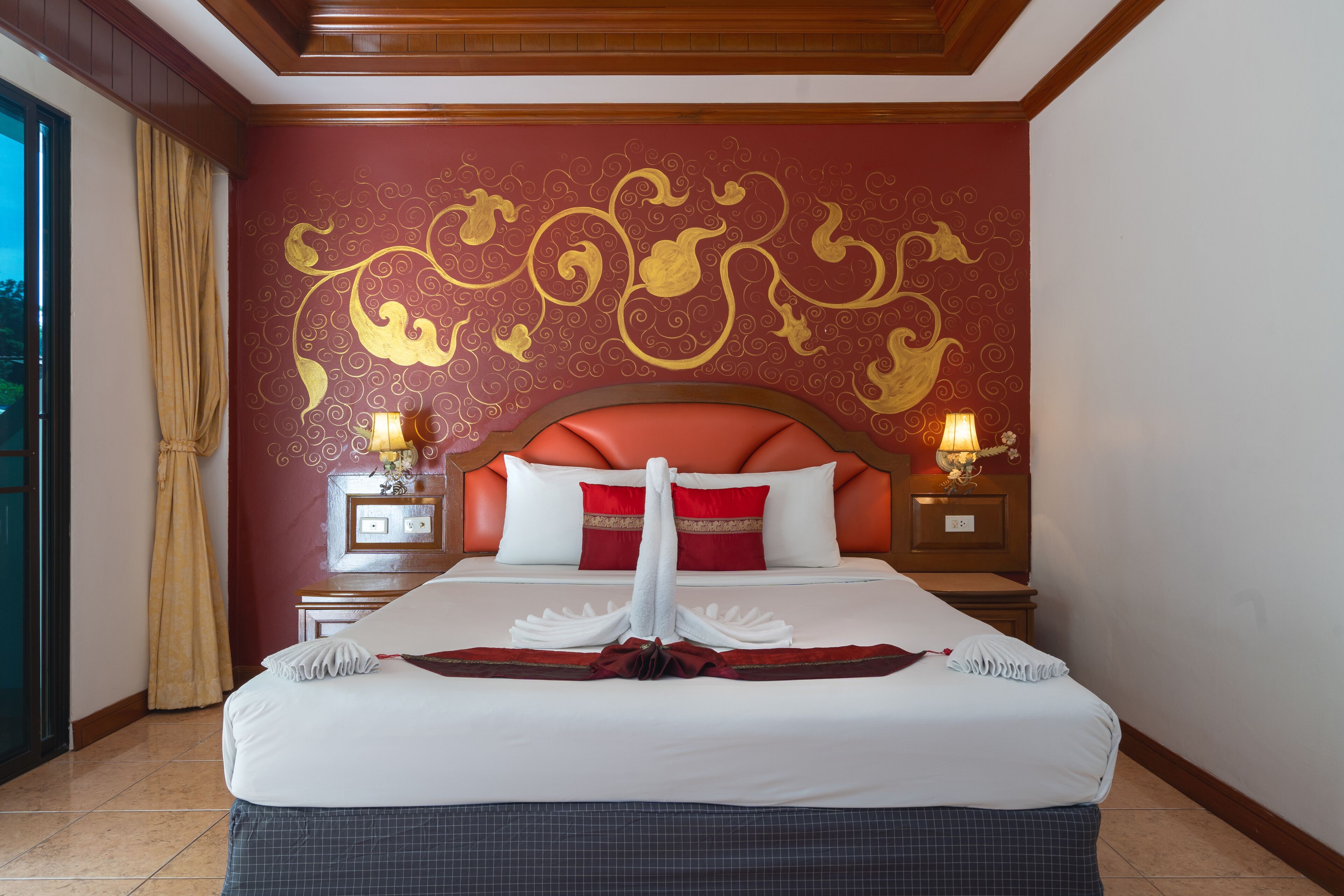 Quarto de hotel com uma cama grande, cabeceira vermelha e arte decorativa na parede. Há duas mesas de cabeceira com abajures.