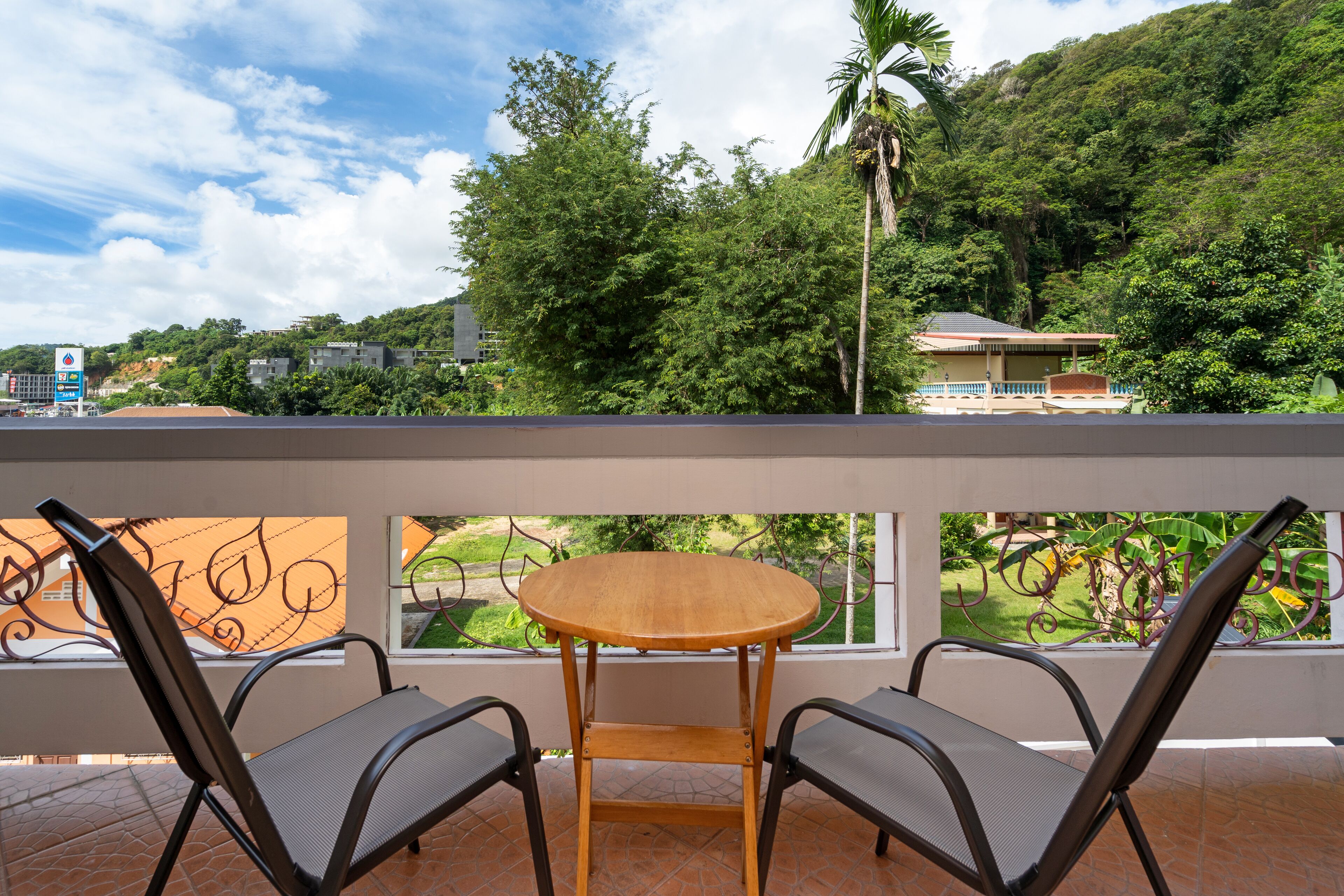 A balcony with two chairs and a small table, overlooking a lush green landscape and a building in the background.