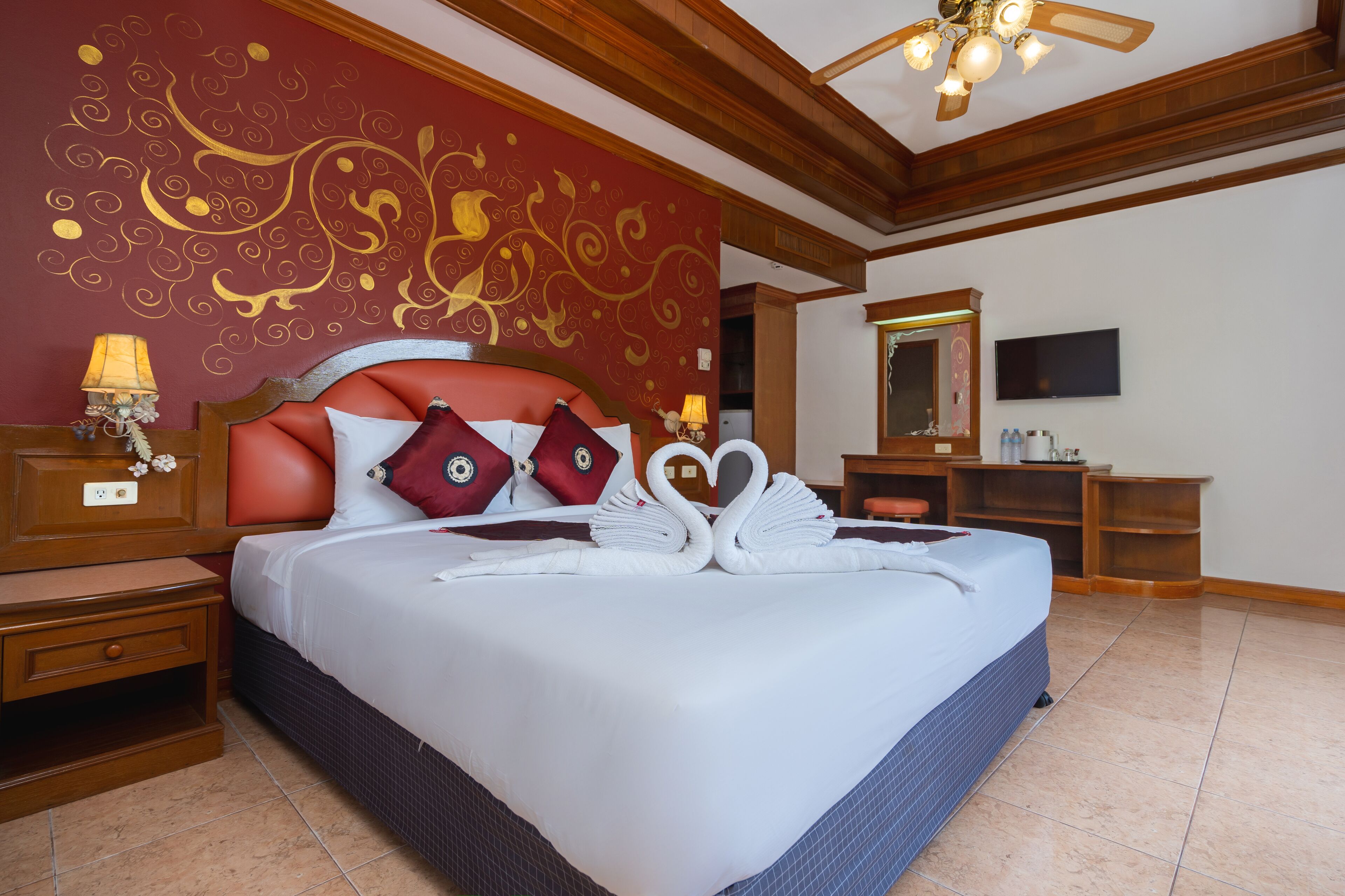 A hotel room with a large bed, a wooden headboard, a TV, a desk, and a mirror.