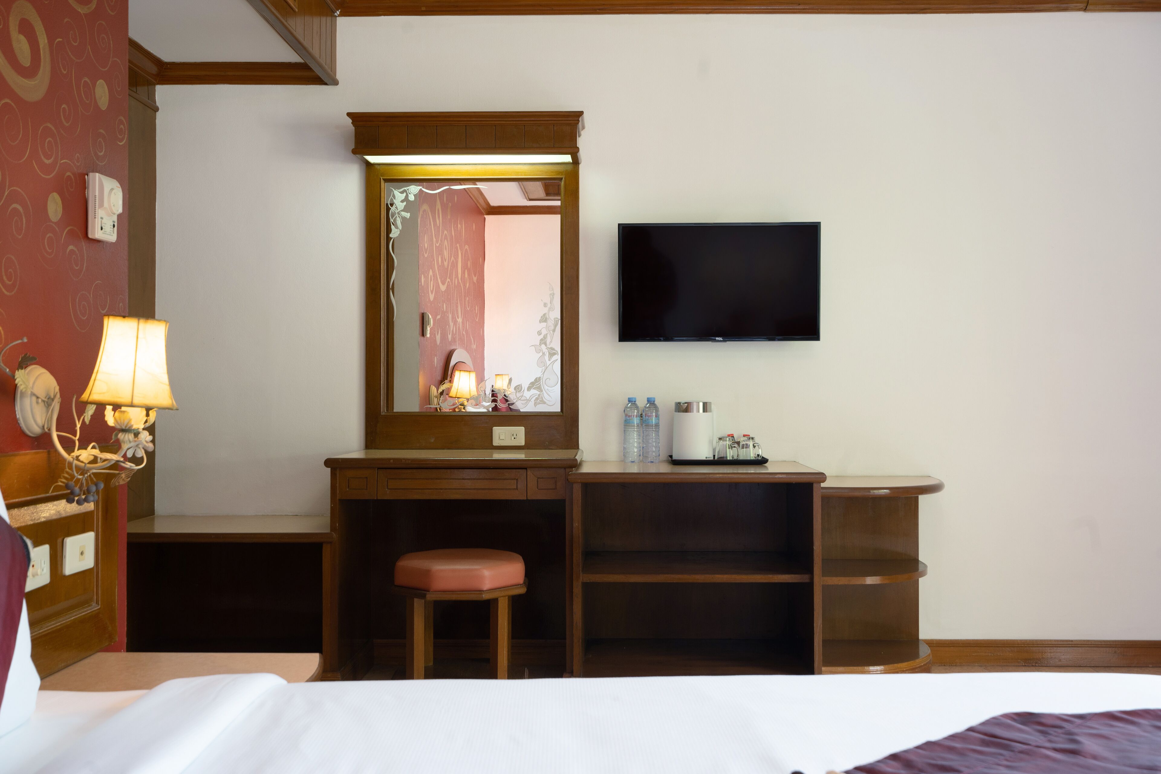 Une chambre d’hôtel comprenant un lit, un bureau avec une chaise, une télévision, un miroir et une étagère avec des bouteilles.