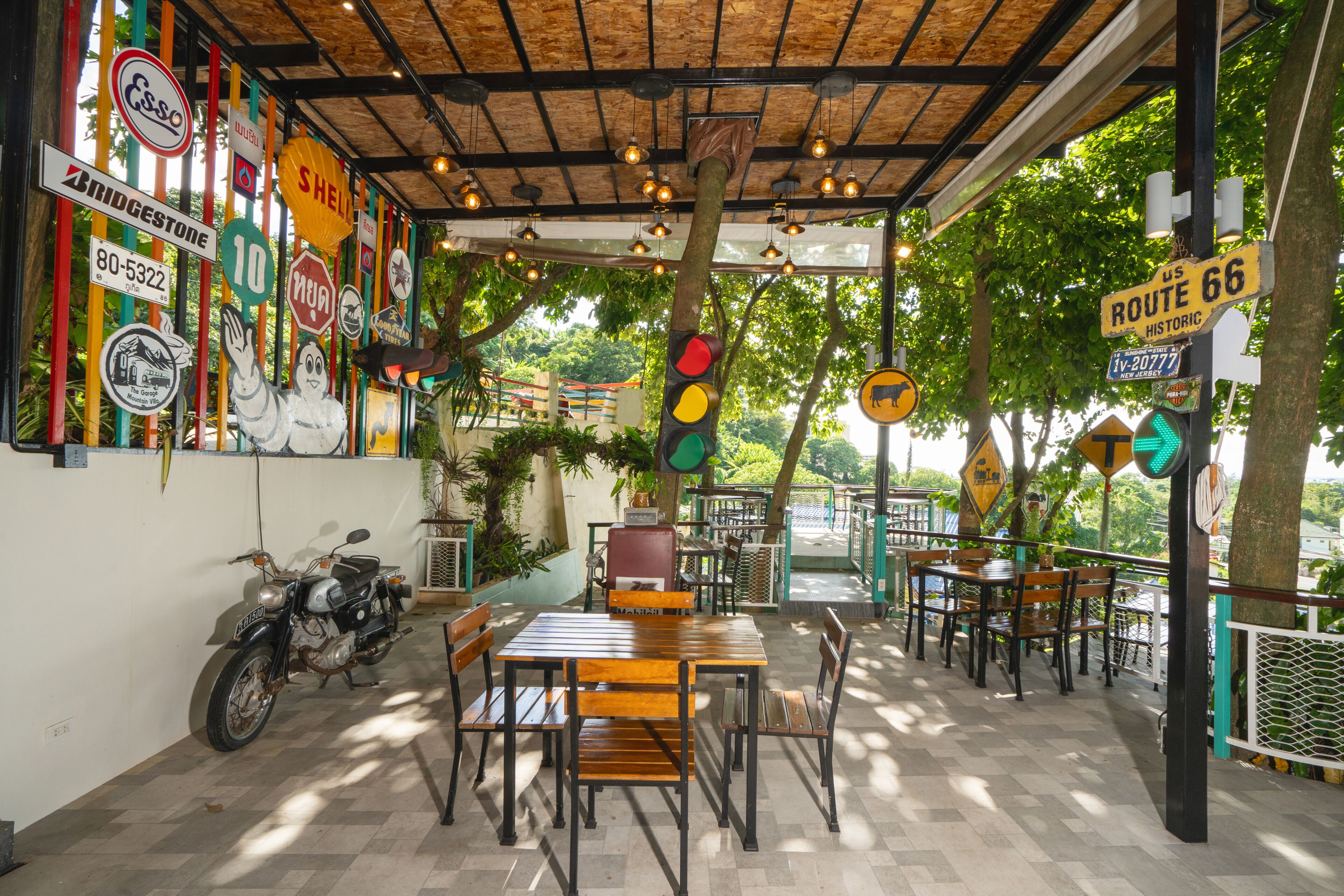 An outdoor cafe with wooden tables and chairs, a motorcycle parked to the side, and various road signs on the walls.