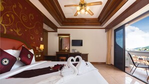 A hotel room with a bed featuring a swan towel arrangement, a television on the wall, a desk with a chair, and a balcony with a view. - Memory Karon Resort (Karon)