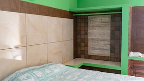 Um quarto com uma cama, um banquinho e uma parede verde.