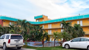 Um hotel com vários andares, fachada amarela e detalhes em azul, com piscina e palmeiras.