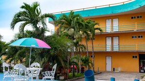 Um hotel com área de estar ao ar livre em azul e branco, palmeiras e fachada de edifício amarela.