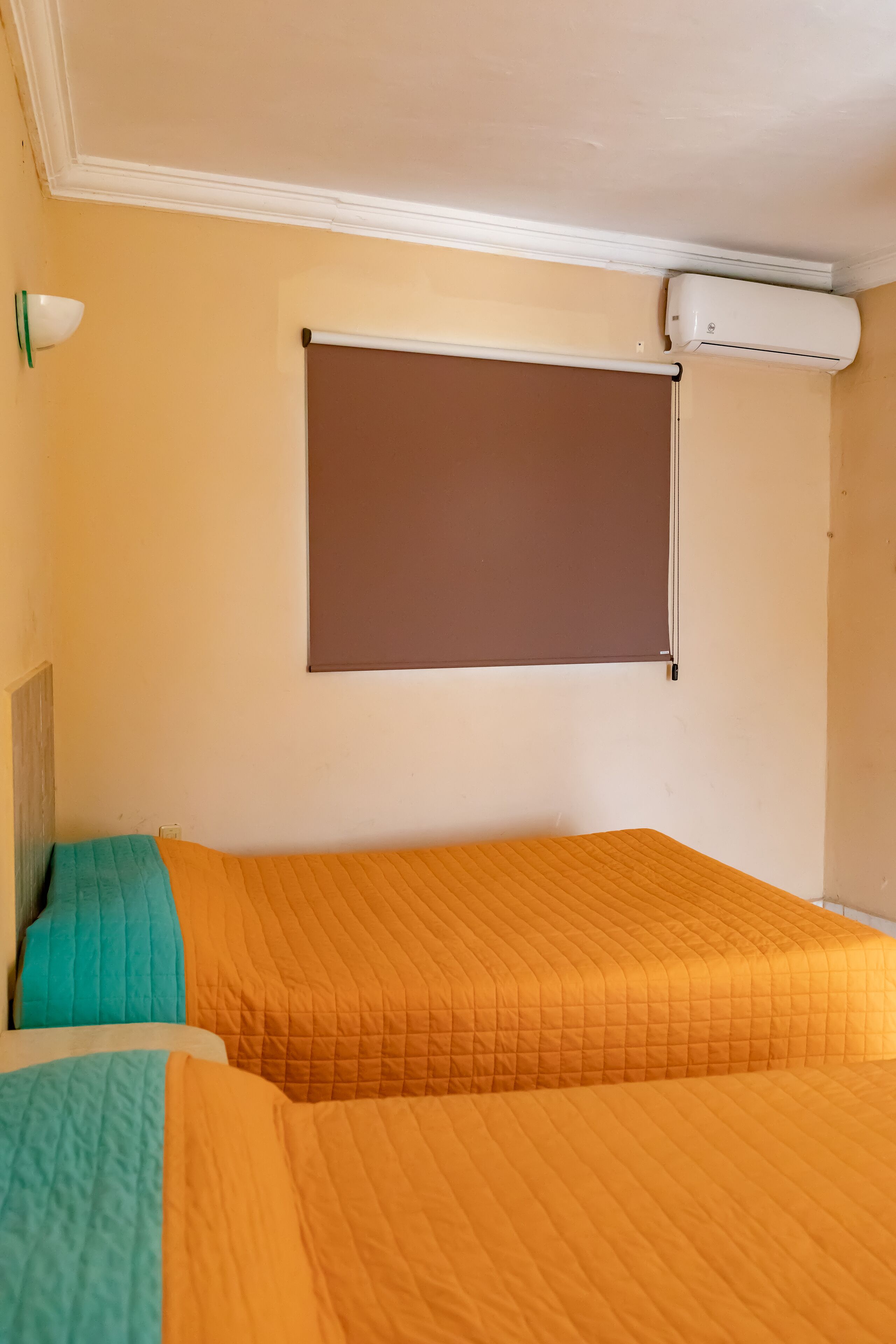 A room with two beds, a ceiling fan, a window with a blind, and a wall-mounted air conditioner.