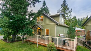Une maison à deux étages avec une terrasse, entourée d’arbres.