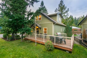 A two-story house with a deck, surrounded by trees.