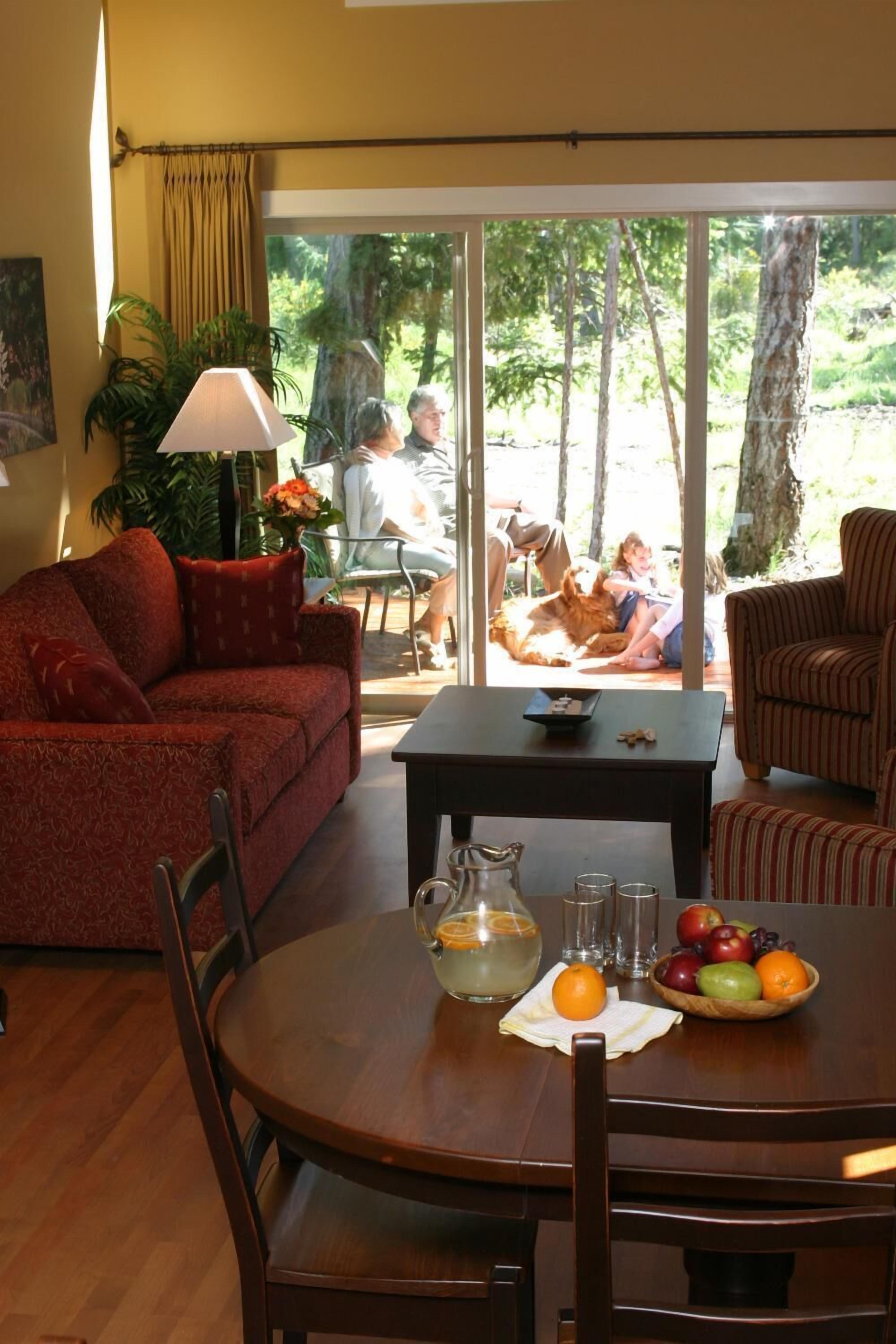 A living room with a sofa, armchairs, a coffee table, and a dining table with fruit and a pitcher.