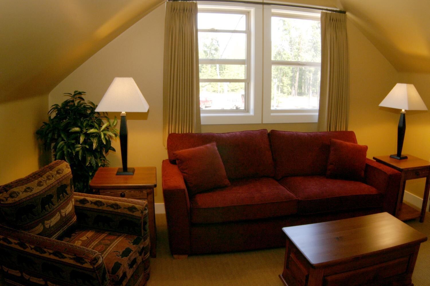 Una sala de estar acogedora con un sofá rojo, dos lámparas a juego, un sillón estampado y una mesa de centro de madera.