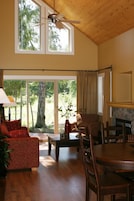 A spacious living room with a high ceiling, large windows, a fireplace, and a dining area.