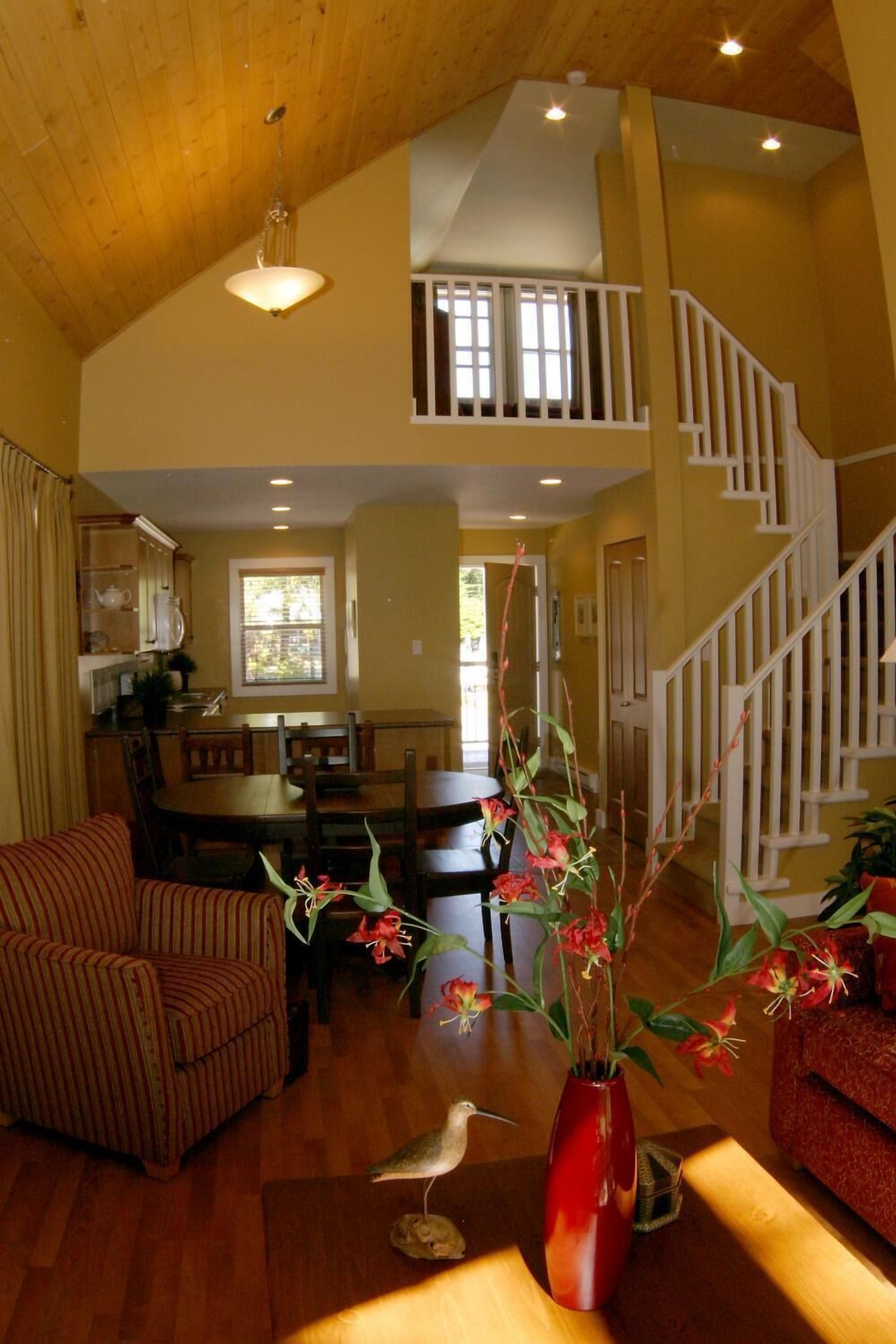 A spacious living area with a wooden ceiling, a dining table, a sofa, and a staircase.