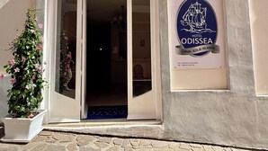 L’entrée d’un hôtel, avec une enseigne indiquant « Hôtel Odisea », un pot de fleurs et un sol pavé de pierres.