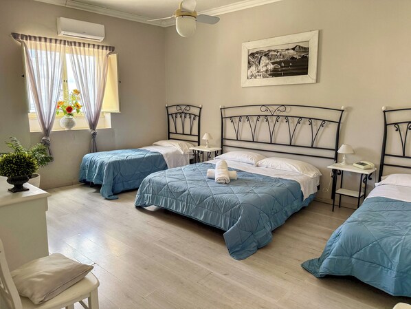A hotel room with two beds, a ceiling fan, a framed picture on the wall, and a window with curtains. - Hotel Odissea (Lipari)