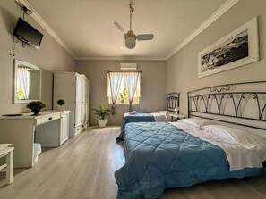 Ein Schlafzimmer mit zwei Betten, einem Deckenventilator, einem Schreibtisch mit Computer, einem Kleiderschrank und einem Fenster mit Vorhängen.