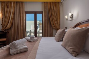Habitación de hotel con cama, toallas, cortinas, vista al balcón y una lámpara de pared.