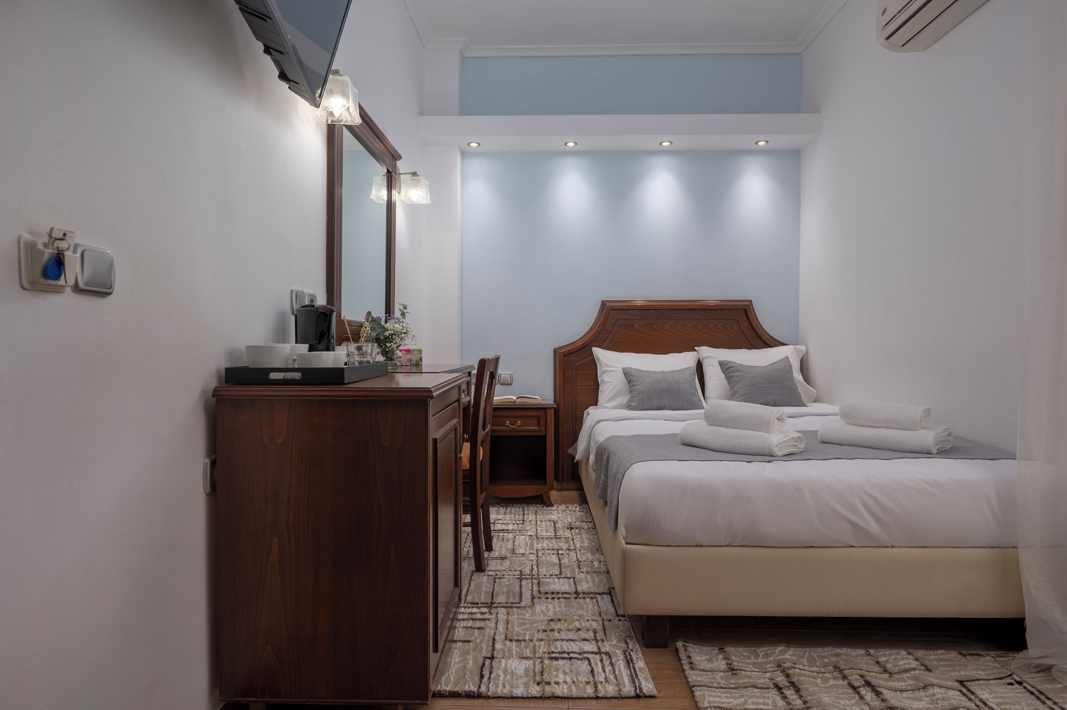 Een slaapkamer met een bed, nachtkastje, spiegel, kaptafel en een klein bureau met stoel.