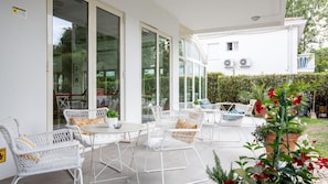An outdoor patio with white wicker furniture and a glass door leading to a covered area. - Villa Rosa BeYou Hotel (Riccione)