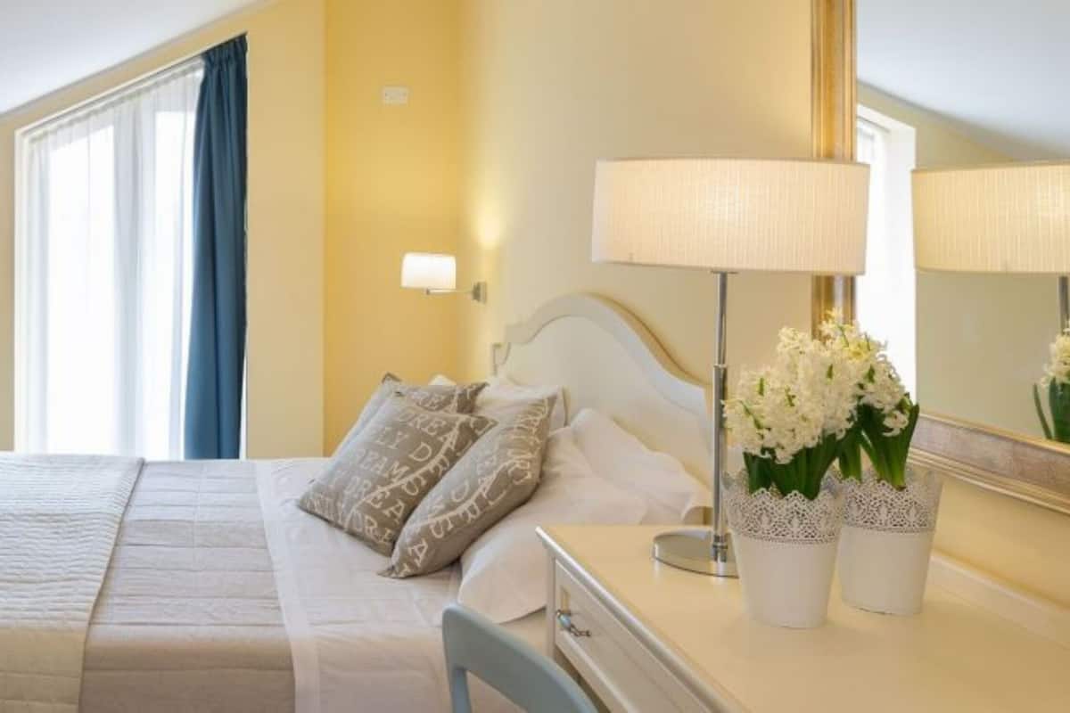 A hotel room with a bed, bedside table, lamp, and flowers.