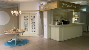 A reception area with a 'Welcome' sign, a reception desk, a blue rug, and a decorative table with flowers.