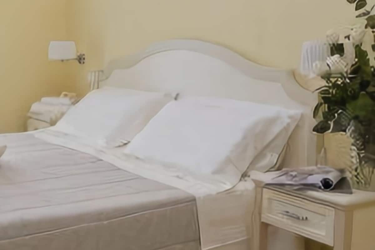 A neatly made bed with white linens and pillows, a bedside table with a lamp, and a small plant on the nightstand.