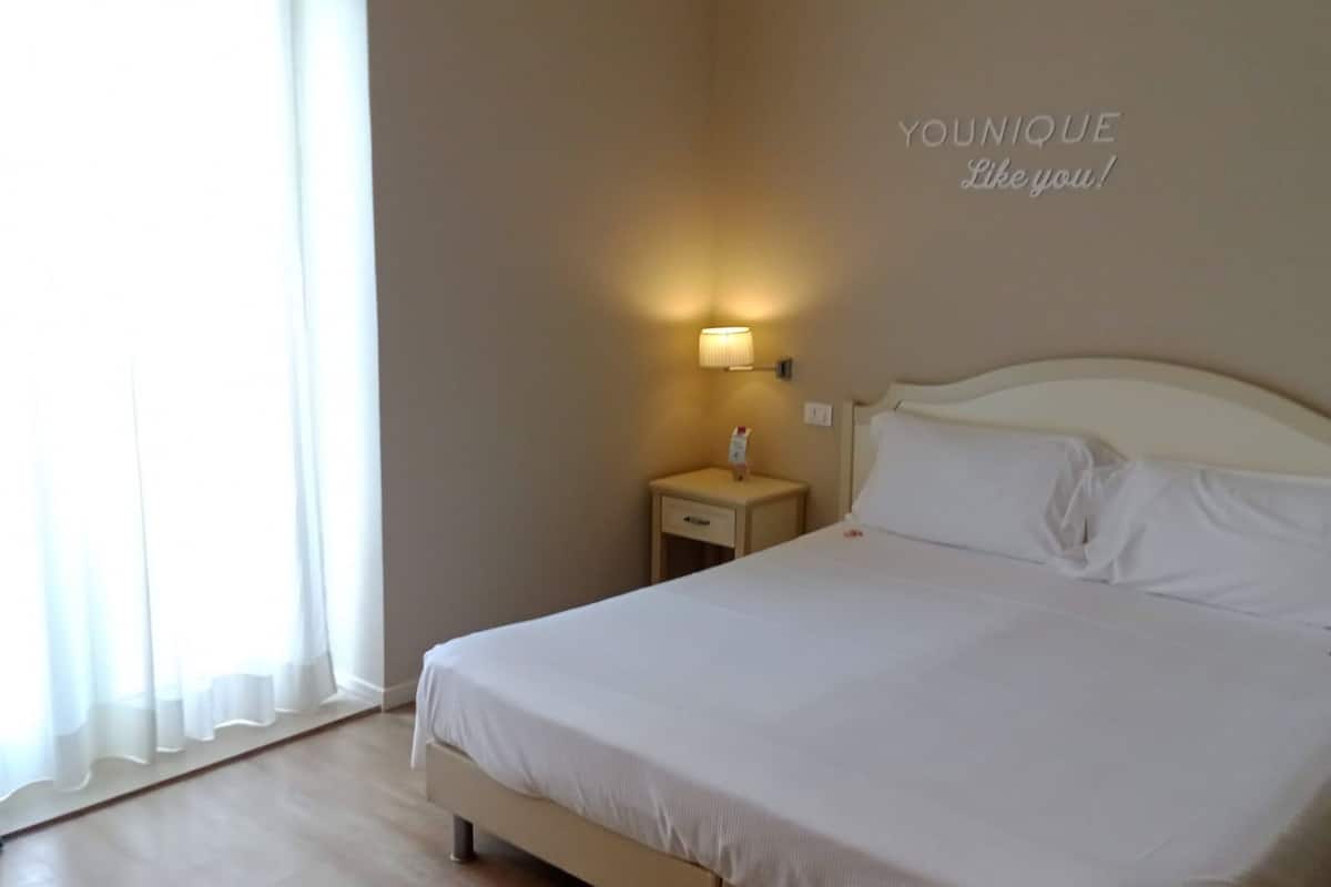 A hotel room with a bed, a bedside table, a lamp, and a wall with the text "YOUNIQUE Like you!".