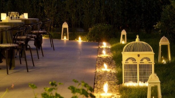 An outdoor dining area with tables and chairs, surrounded by a pathway lined with candles and lanterns.
