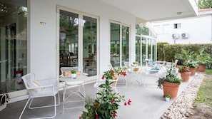 An outdoor patio with white furniture, potted plants, and a glass door entrance. - Villa Rosa BeYou Hotel (Riccione)