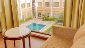 A room with a view of a swimming pool, a sofa, and a small table. - Tivoli Garden Resort (New Delhi)