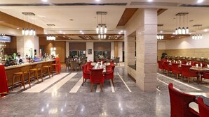 A spacious restaurant with multiple dining areas, a bar, and a counter with a variety of items. - Tivoli Garden Resort (New Delhi)