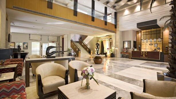 A spacious lobby with a high ceiling, a reception desk, and a staircase leading to an upper level. - Tivoli Garden Resort (New Delhi)