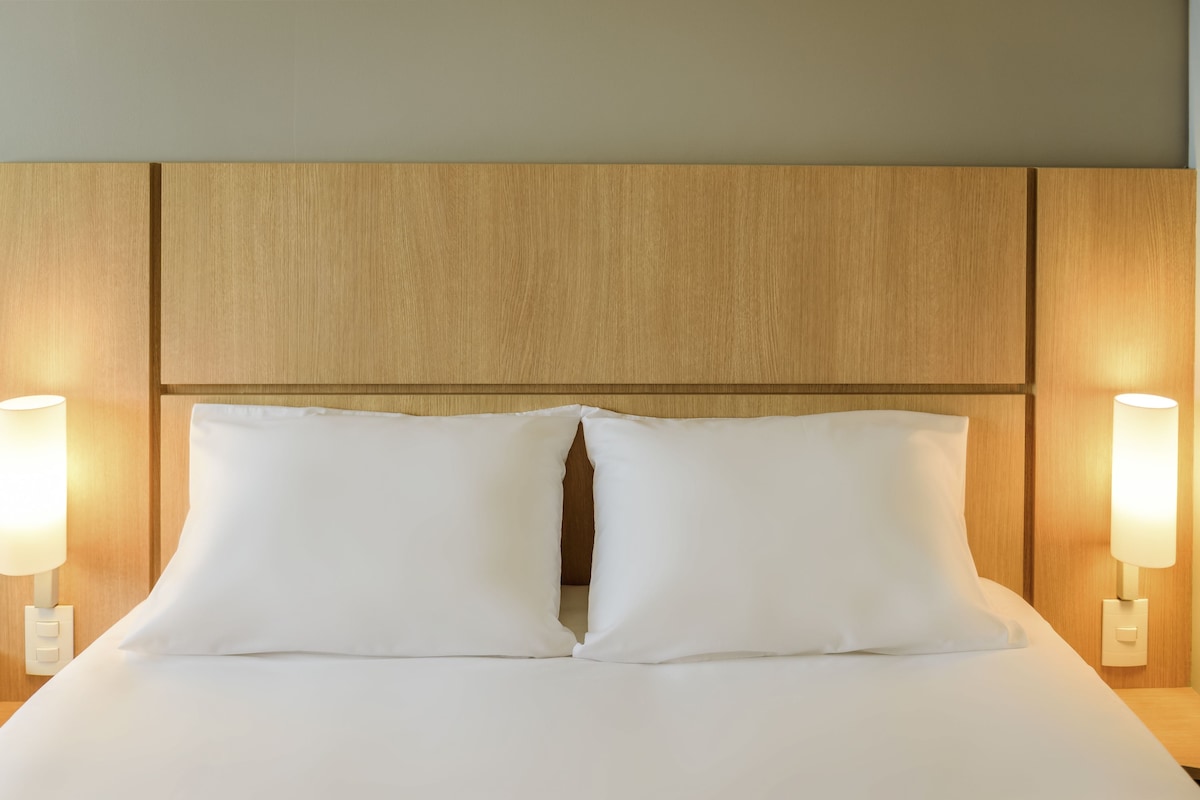A neatly made bed with white linens and two pillows, flanked by two wall-mounted lamps.