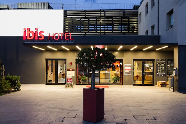 El exterior del hotel ibis, con una fachada moderna, amplias ventanas de vidrio y un llamativo letrero rojo.