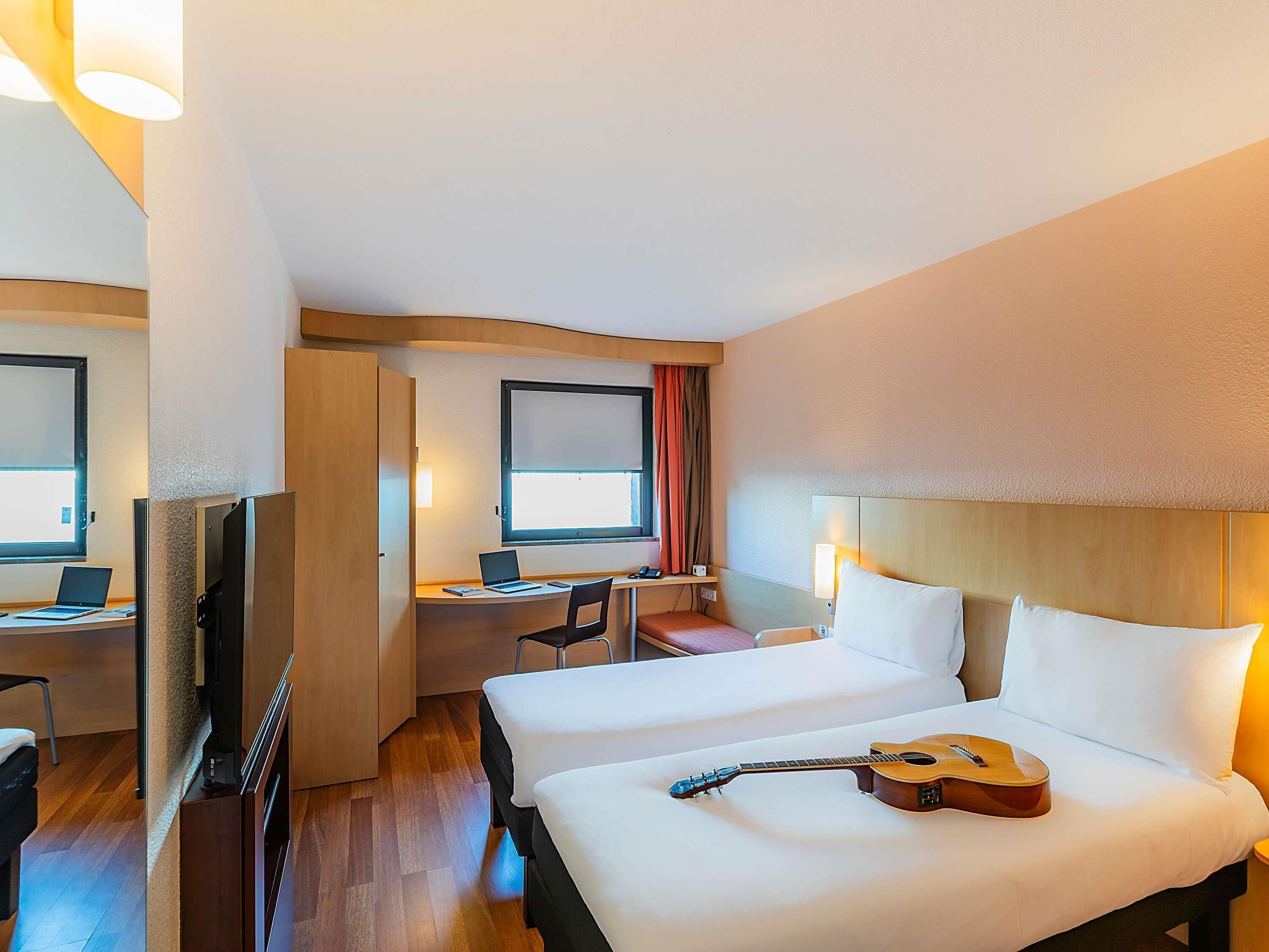 Une chambre d’hôtel avec deux lits, un bureau avec un ordinateur portable, une télévision et une guitare posée sur l’un des lits.