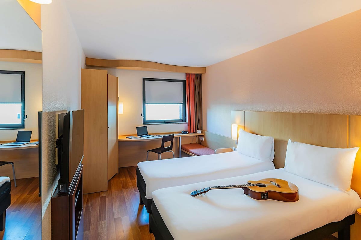 Une chambre d’hôtel avec deux lits, un bureau avec un ordinateur portable, une télévision et une guitare posée sur l’un des lits.
