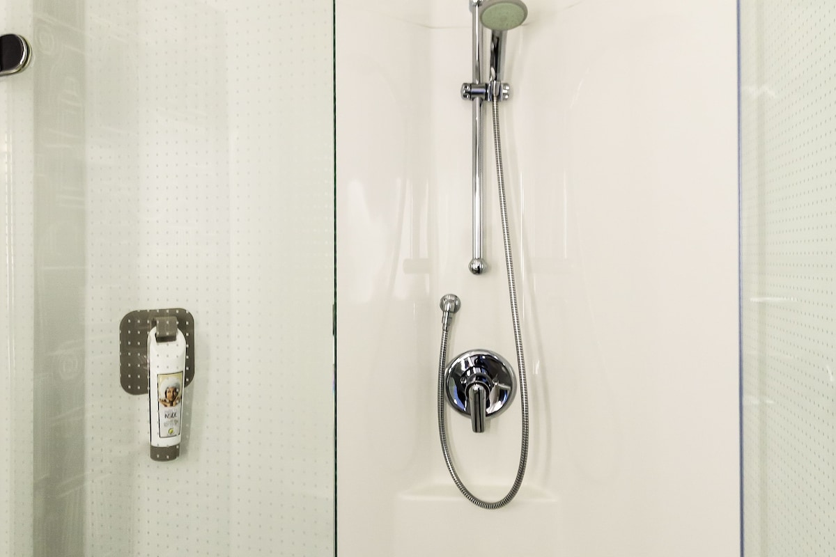 A bathroom with a shower, a towel rack, and a soap dispenser.