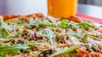 Pizza con diferentes ingredientes y un vaso de zumo de naranja sobre una mesa.