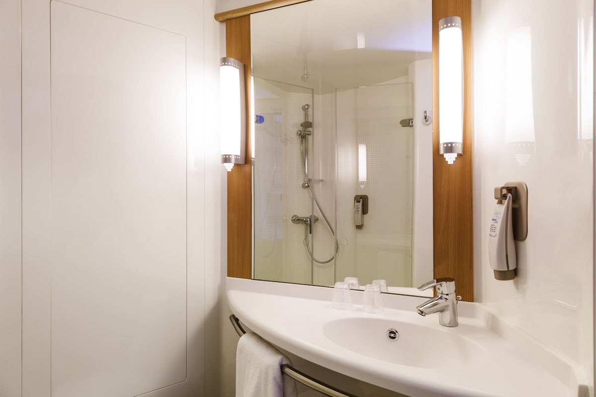 A modern bathroom with a white sink, a glass shower enclosure, and a mirror with wooden frame.