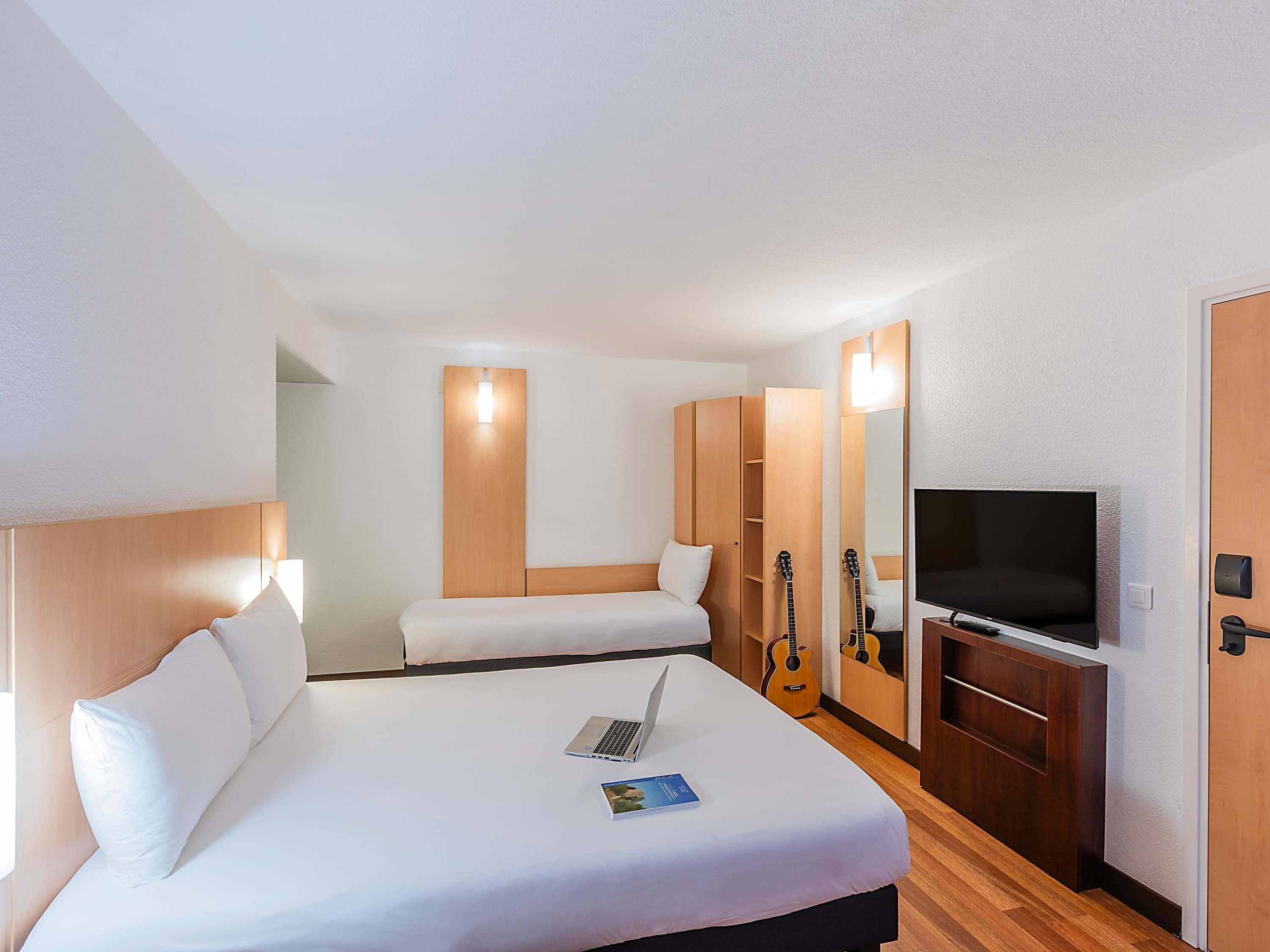 Habitación de hotel con cama, escritorio con computadora portátil, televisión y guitarra.