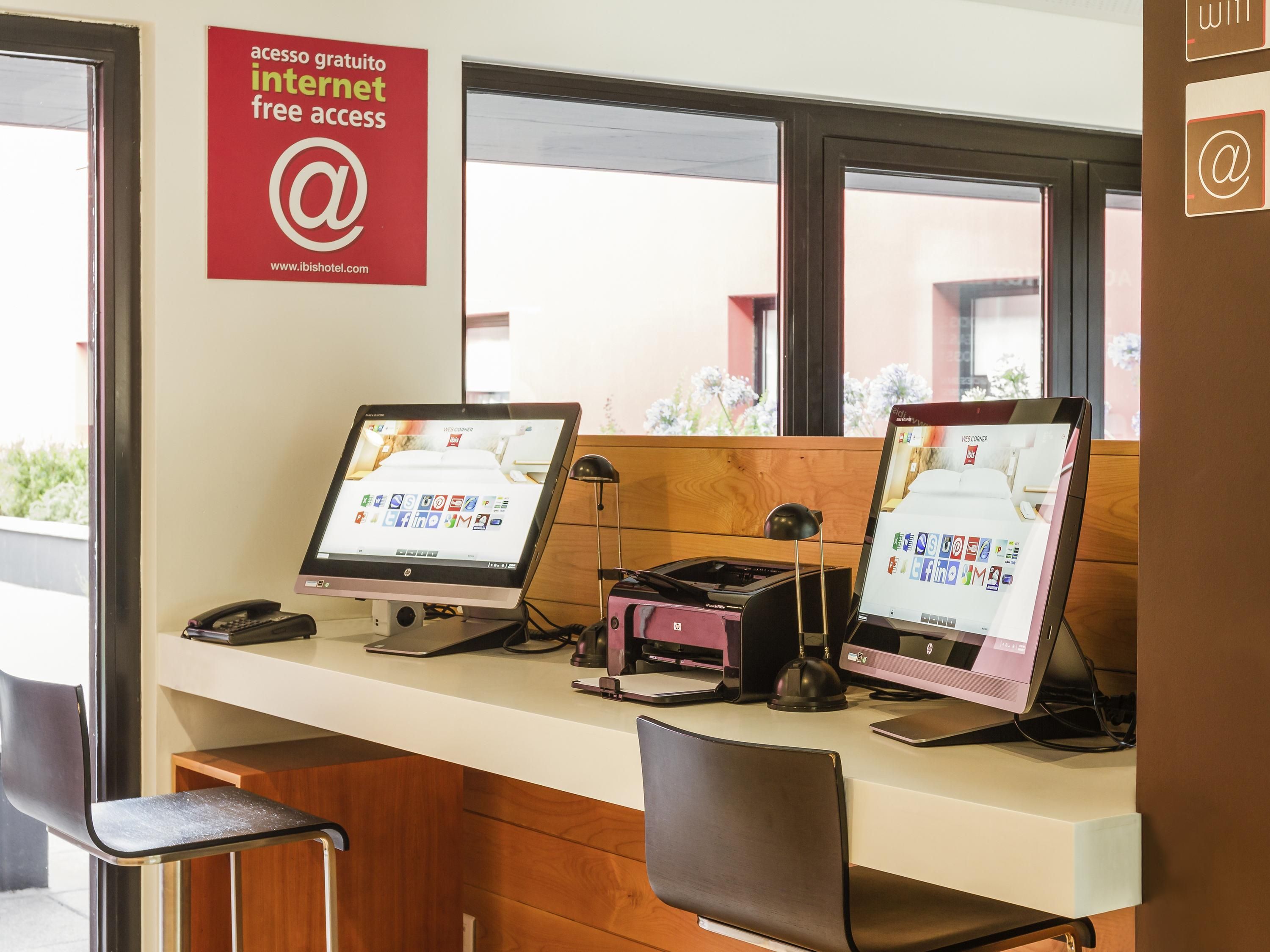 Un comptoir d’accueil d’hôtel équipé de deux ordinateurs HP, d’un téléphone et d’un panneau indiquant un accès gratuit à Internet.