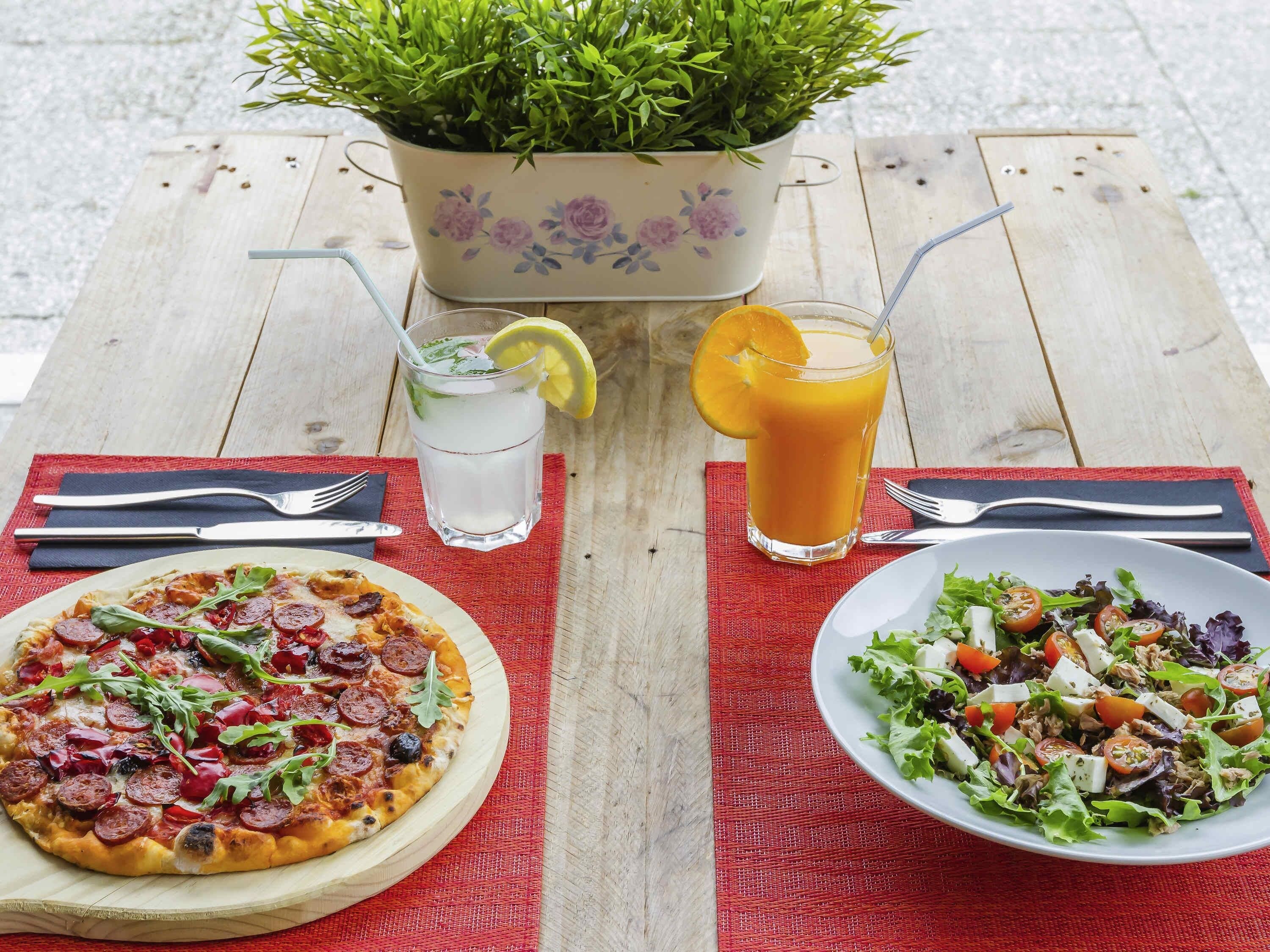 A wooden table with a pizza, a salad, a drink, and a potted plant.