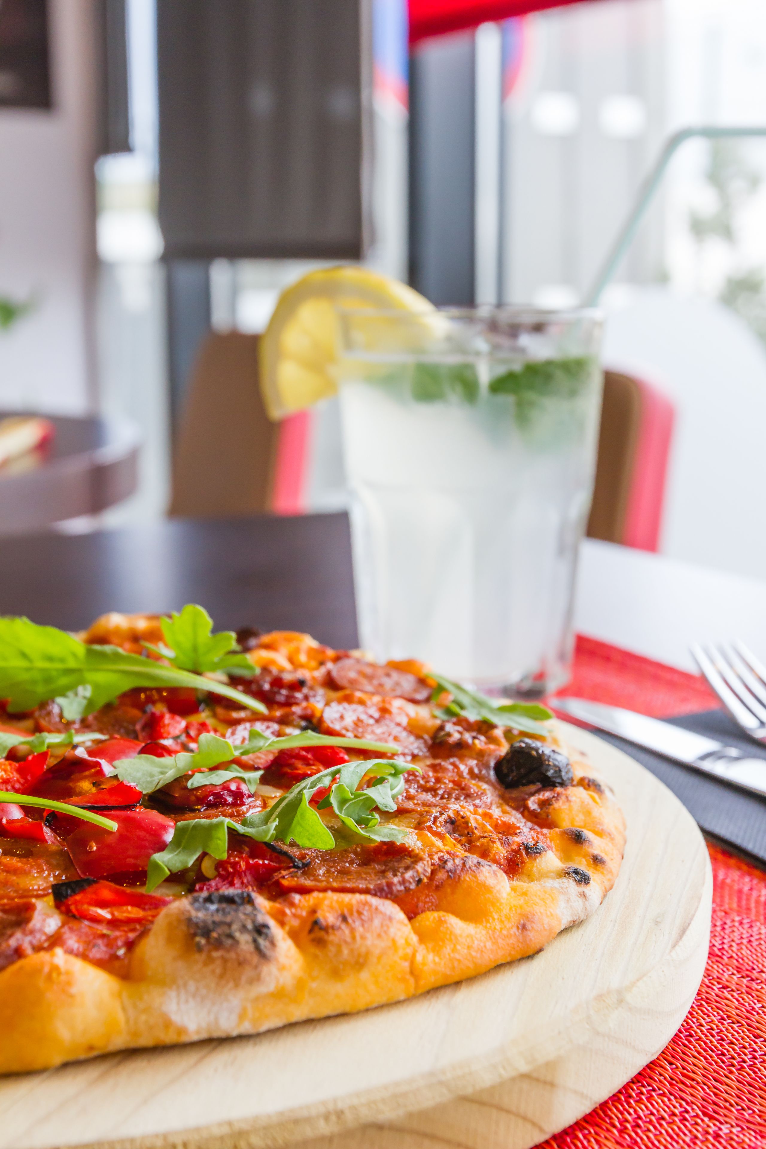 Pizza op een houten plank met een glas ijsthee en een citroenpartje op tafel.
