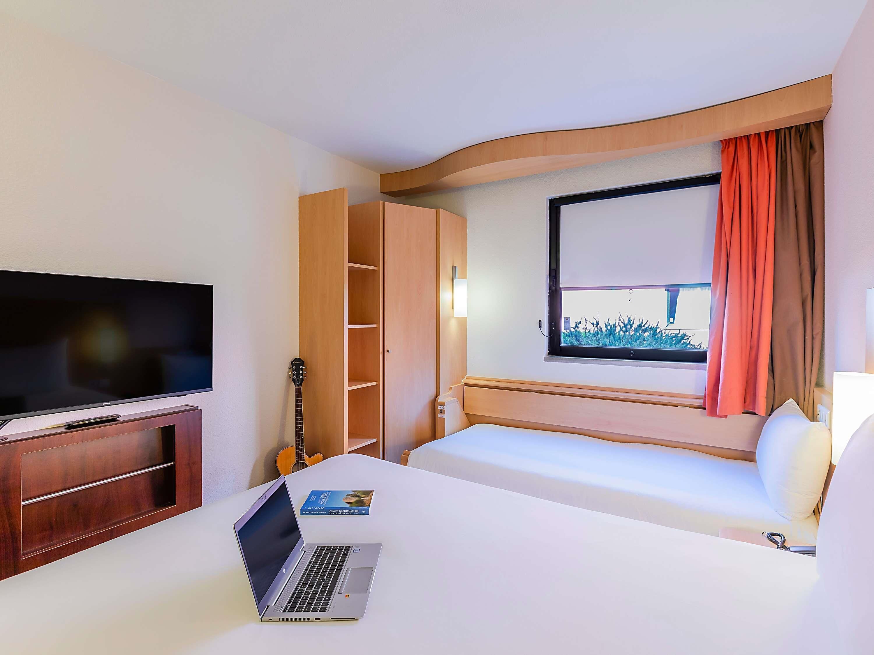 Une chambre d’hôtel avec un lit, une télévision, un ordinateur portable, une guitare et une fenêtre avec des rideaux.