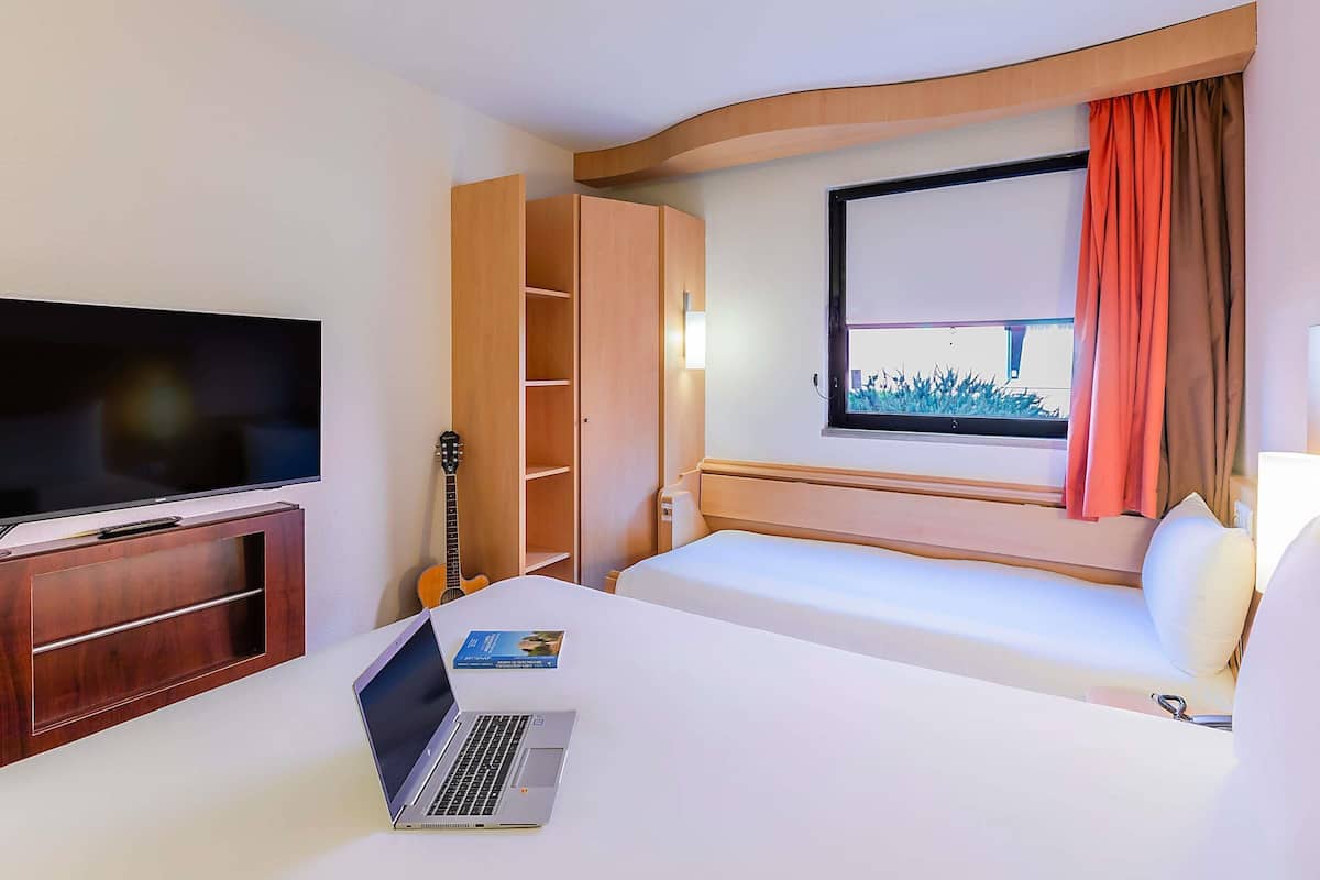 Une chambre d’hôtel avec un lit, une télévision, un ordinateur portable, une guitare et une fenêtre avec des rideaux.