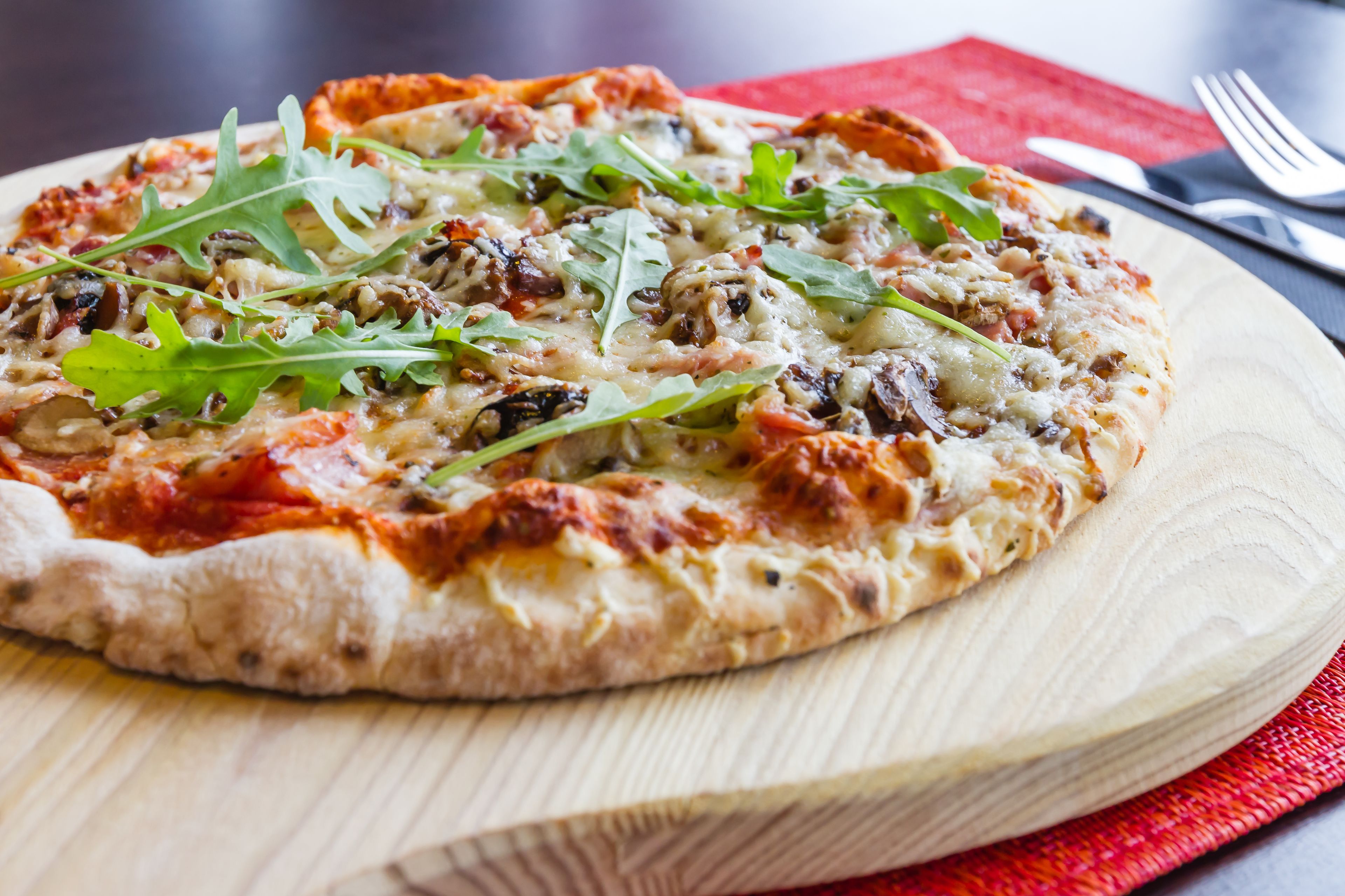 Une pizza servie sur une planche en bois, avec une serviette rouge placée en dessous.