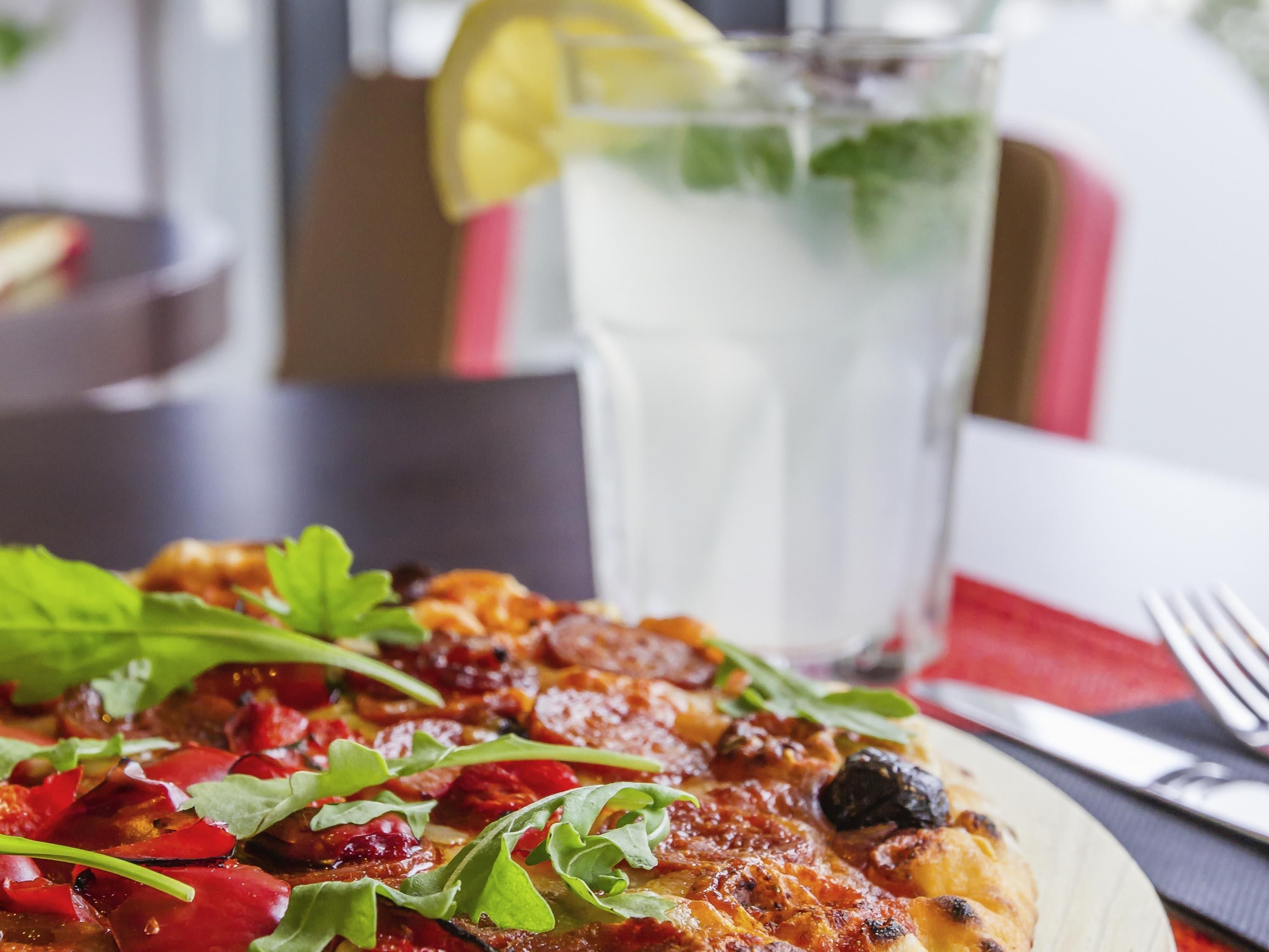 A pizza with toppings and a glass of iced beverage on a table.