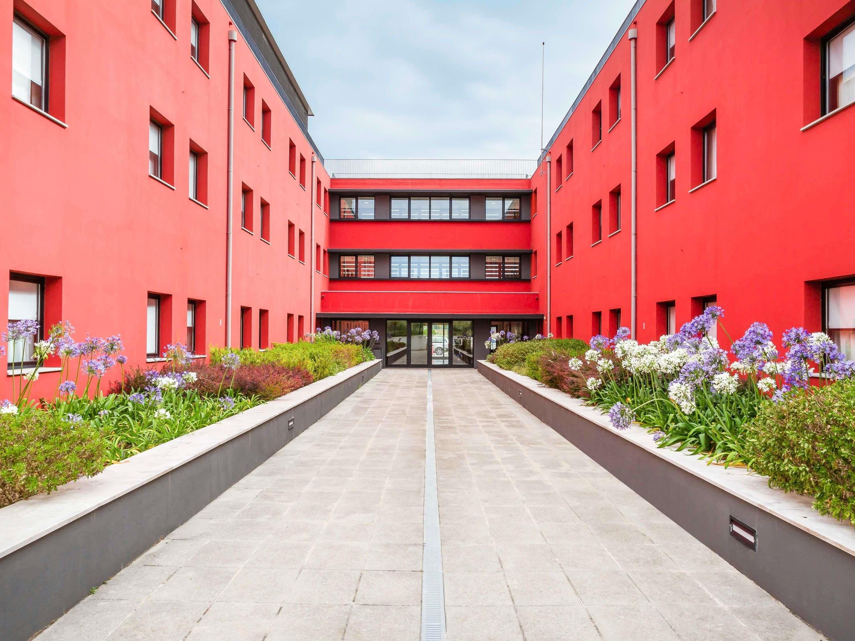 A modern building with a red facade, a central entrance, and a symmetrical design.